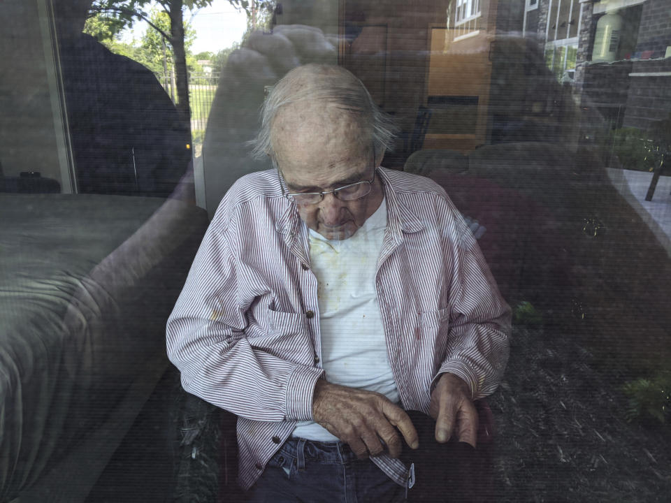 This June 7, 2020, photo provided by June Linnertz shows her father, James Gill, seen through a window at Cherrywood Pointe nursing home in Plymouth, Minn. As more than 90,000 of America’s long-term care residents have died in the coronavirus pandemic, advocates for the elderly say a tandem wave of death separate from the virus has quietly claimed tens of thousands more, often because overburdened workers haven’t been able to give them the care they need. Gill died of Lewy Body Dementia, according to a copy of his death certificate provided to the AP. Linnertz always expected her father to die of the condition, which causes a progressive loss of memory and movement, but never thought he would end his days in so much needless pain. (June Linnertz via AP)