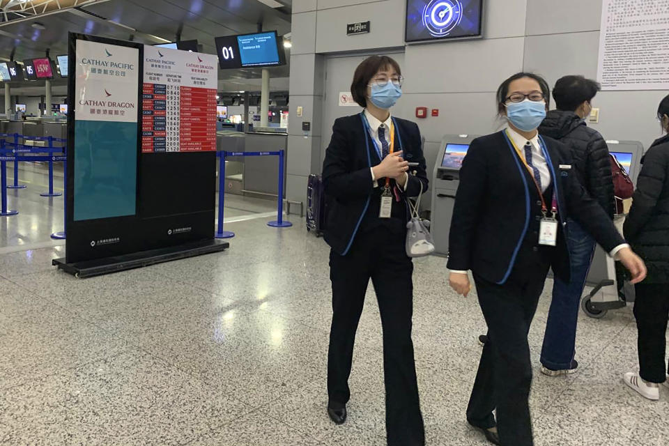 Staff members wearing face masks walk near the check in counters for Cathay Pacific at Shanghai Pudong International Airport in Shanghai, Thursday, Jan. 30, 2020. China counted 170 deaths from a new virus Thursday and more countries reported infections, including some spread locally, as foreign evacuees from China's worst-hit region returned home to medical observation and even isolation. (AP Photo/Erika Kinetz)