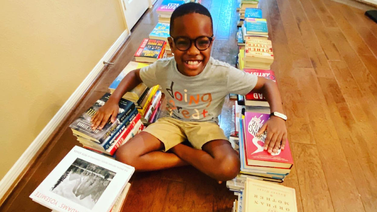 Orion smiles while seated cross-legged on the floor between two rows of books.