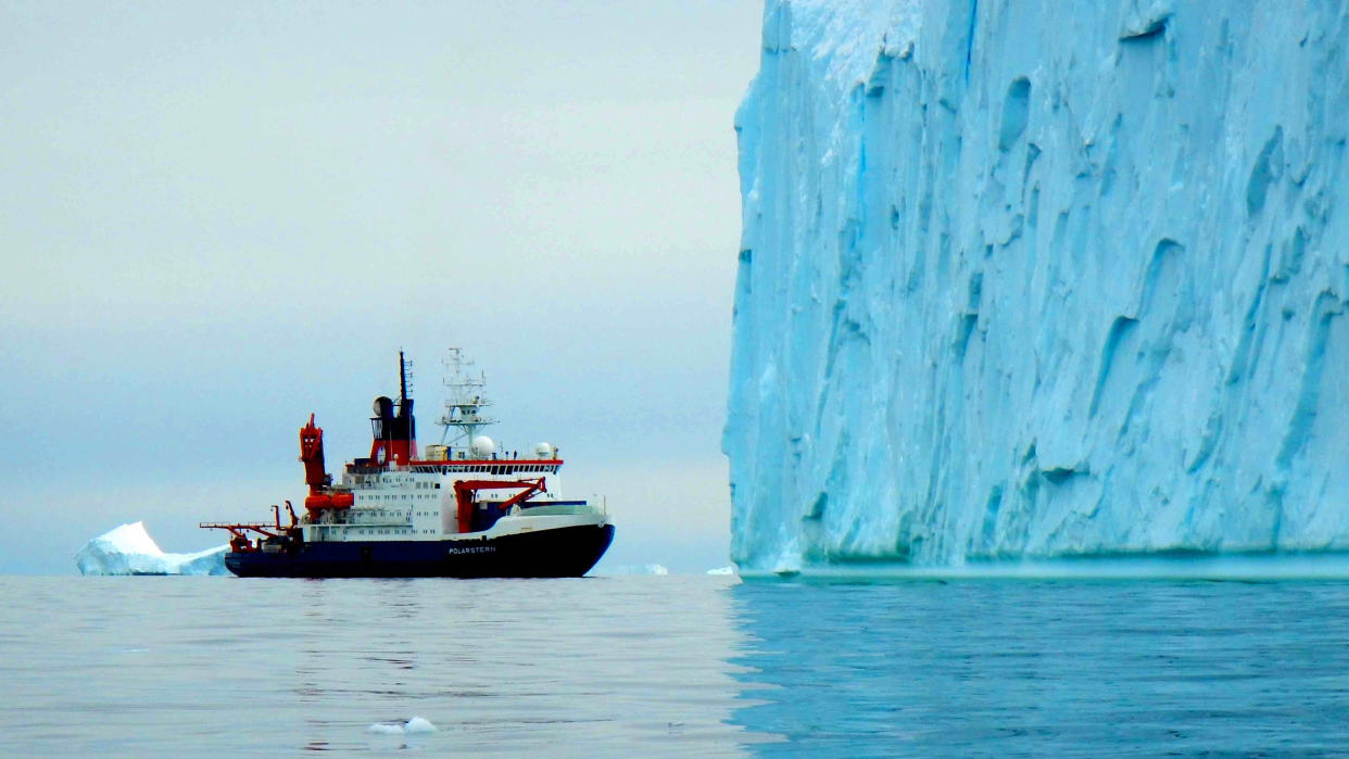  A research vessel in front of a massive iceberg. 