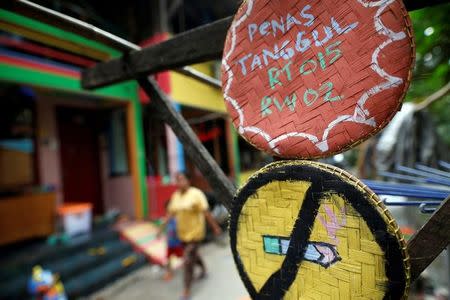 A woman and child walk near a no smoking sign hanging in a poor riverside neighborhood where locals have recently painted their homes in bright colours to encourage residents to stop smoking and promote a smoke-free environment in Penas Tanggul, East Jakarta, Indonesia, May 8, 2017. REUTERS/Darren Whiteside/File photo