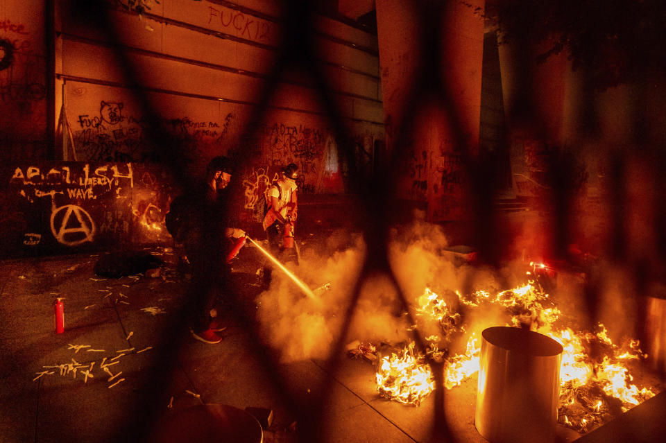 A protester extinguishes a fire set by fellow protesters at the Mark O. Hatfield United States Courthouse on Wednesday, July 22, 2020, in Portland, Ore. Following a larger Black Lives Matter Rally, several hundred demonstrators faced off against federal officers at the courthouse. (AP Photo/Noah Berger)