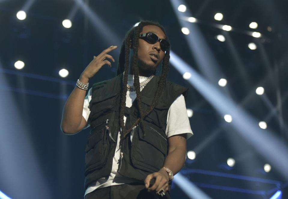 A man with long black hair wearing a black vest and white T-shirt on a stage