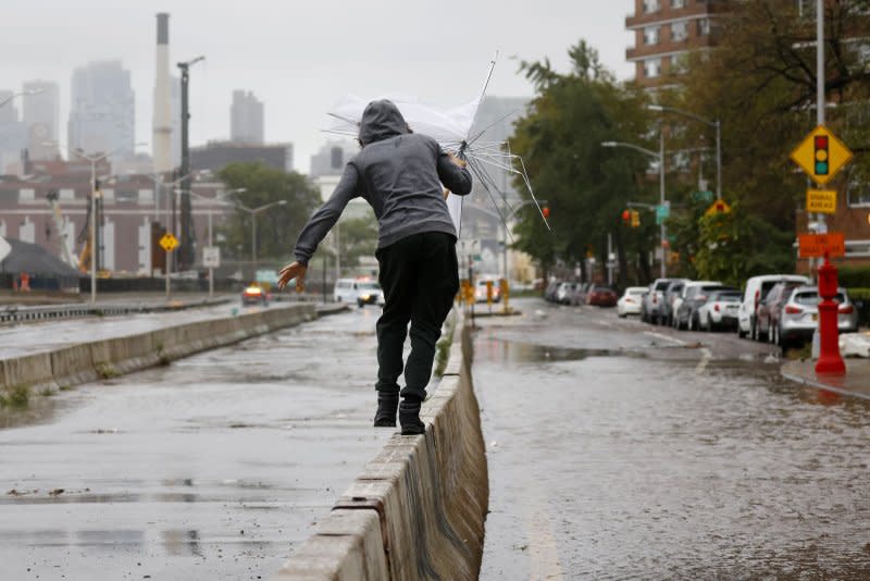 A pedestrian balances while holding an umbrella on a concrete wall divider for separating traffic. Photo by John Angelillo/UPI