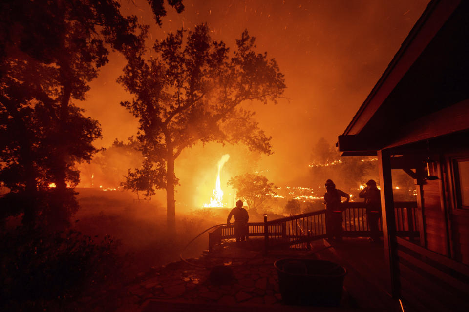 FILE - In this Aug. 21, 2020, file photo, firefighters watch flames from the LNU Lightning Complex fires approach a home in the Berryessa Estates neighborhood of unincorporated Napa County, Calif. The blaze, the fifth largest in California history, forced thousands to flee and destroyed more than 1,000 homes and other structures. This year has seen record Atlantic hurricanes and western wildfires, devastating floods in Asia and Africa and a hot, melting Arctic. It's not just been a disastrous year, but a year of disasters. (AP Photo/Noah Berger, File)