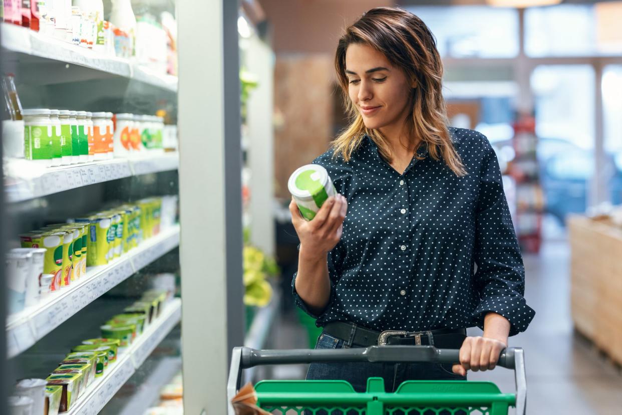 Shot of beauty woman walking with shopping cart while taking products from shelf at the grocery