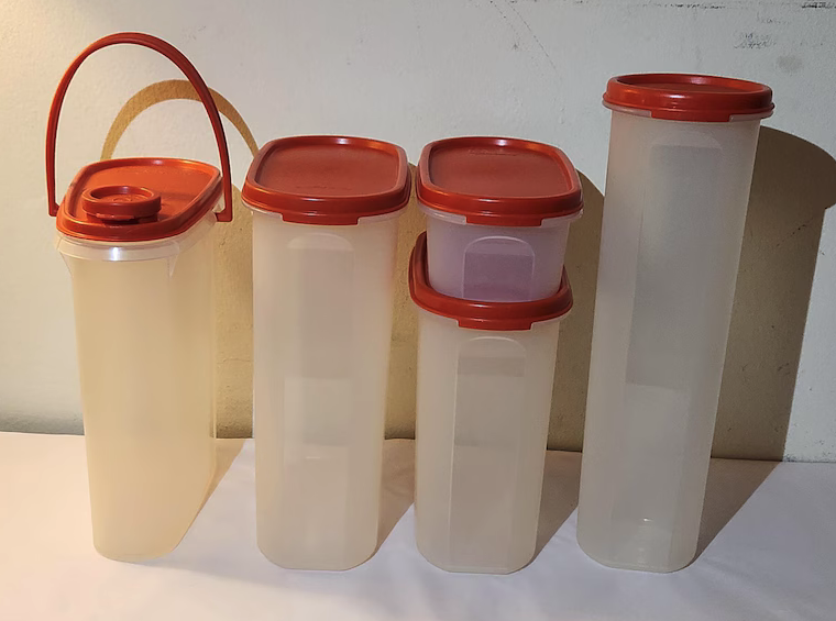 Various translucent storage containers with red lids are displayed on a white surface against a plain backdrop