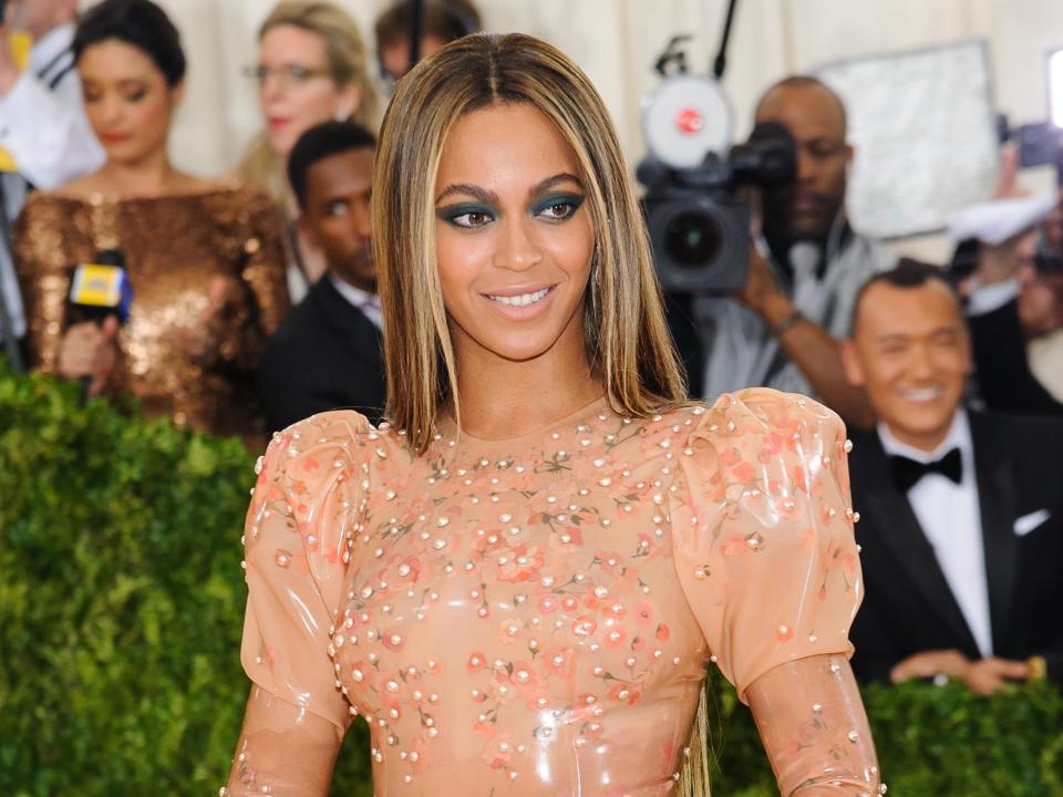 Beyonce smiling in a nude and beaded dress.