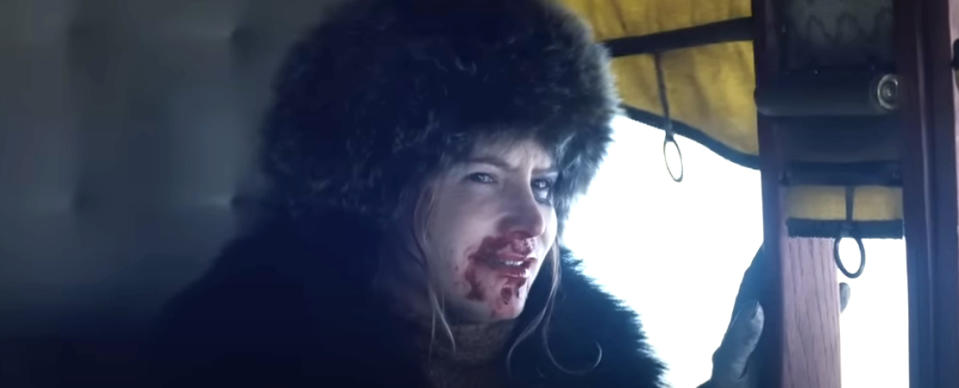 Jennifer Lawrence with blood on her face, dressed in fur clothing, looking towards the camera from inside a dimly lit space