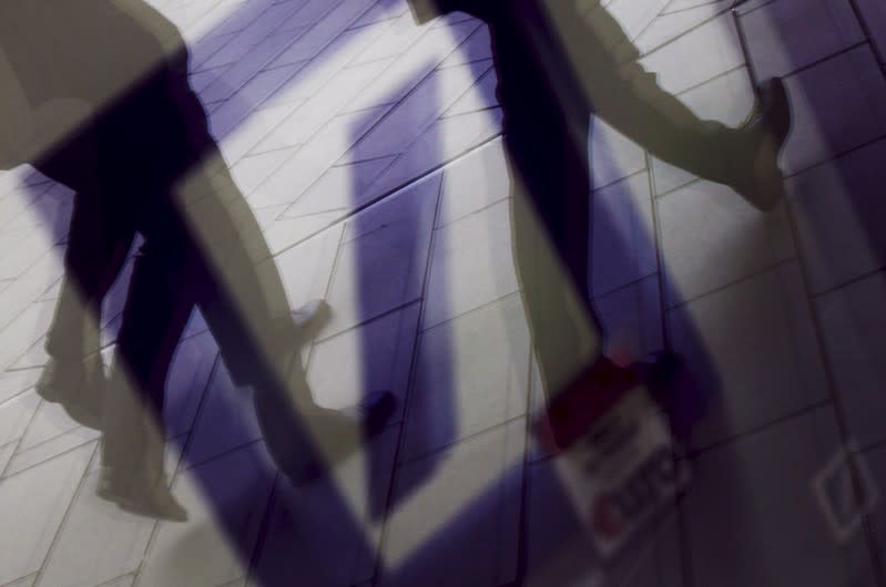 Pedestrians are reflected in a window as they walk in front of the headquarters of Deutsche Bank AG in Frankfurt