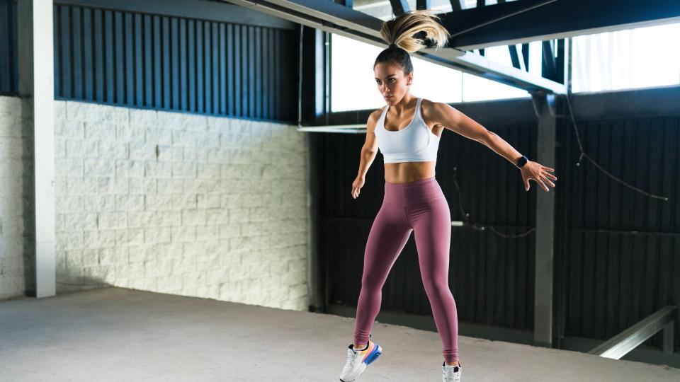 Woman jumping into the air with arms out during HIIT workout