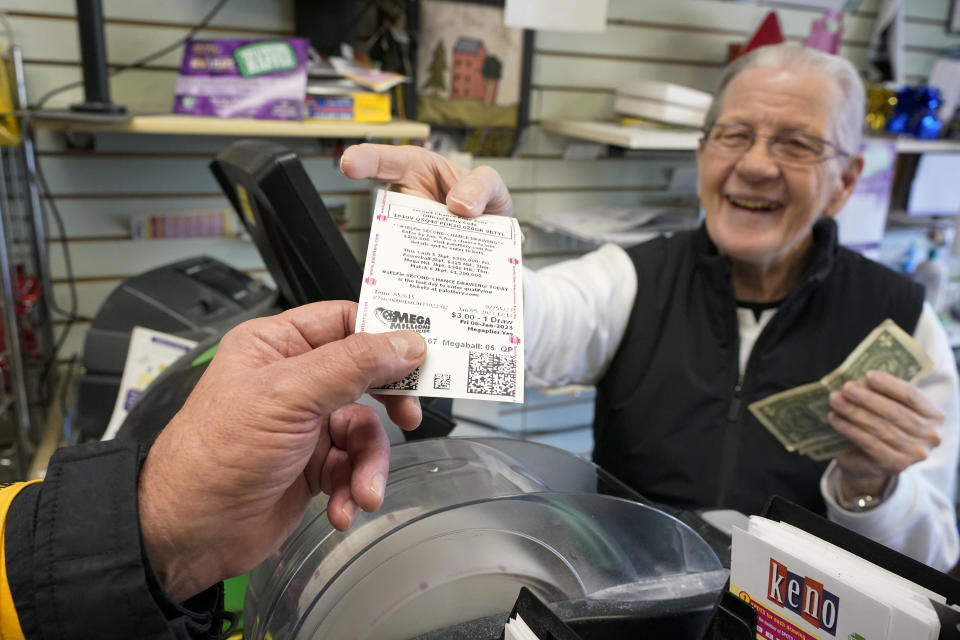 Dot Skoko, owner of Dot's Dollar More or Less shop in Mt. Lebanon, Pa., hands a customer a Mega Millions lottery ticket, Thursday, Jan. 5, 2022. Twenty-three consecutive drawings later with no grand prize winner named, the Mega Millions jackpot is now flirting with nearly $1 billion, making it one of the largest jackpots in lottery history. Thursday, Jan. 5, 2023. (AP Photo/Gene J. Puskar)