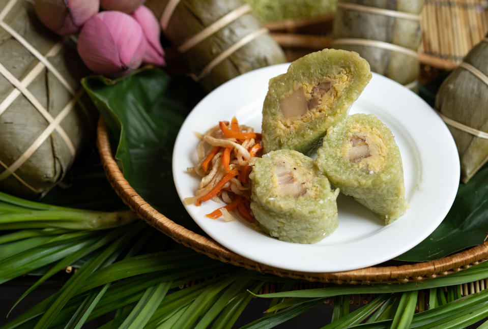 Unwrapped and sliced bánh tét are on a white plate while wrapped bánh tét are in the background