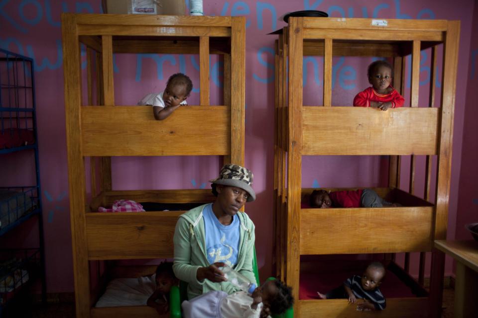 In this Feb. 1, 2014 photo, an orphanage worker feeds a baby at the U.S.-based Church of Bible Understanding-run orphanage in Kenscoff, Haiti. The religious group sells expensive antiques at high-end stores called Olde Good Things in New York and Los Angeles and says it uses a portion of the profit to fund the orphanage. (AP Photo/Dieu Nalio Chery)