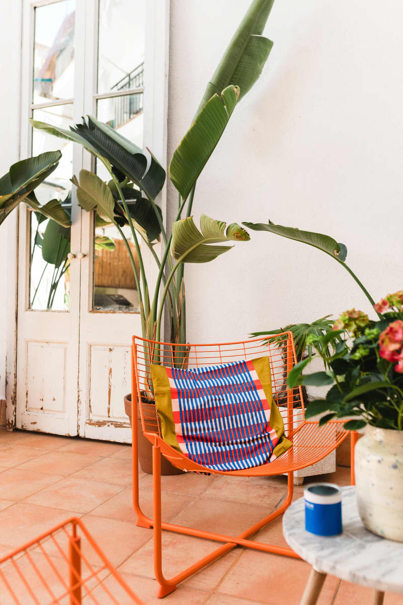 White outdoor area with lots of plants, small table with orange chairs