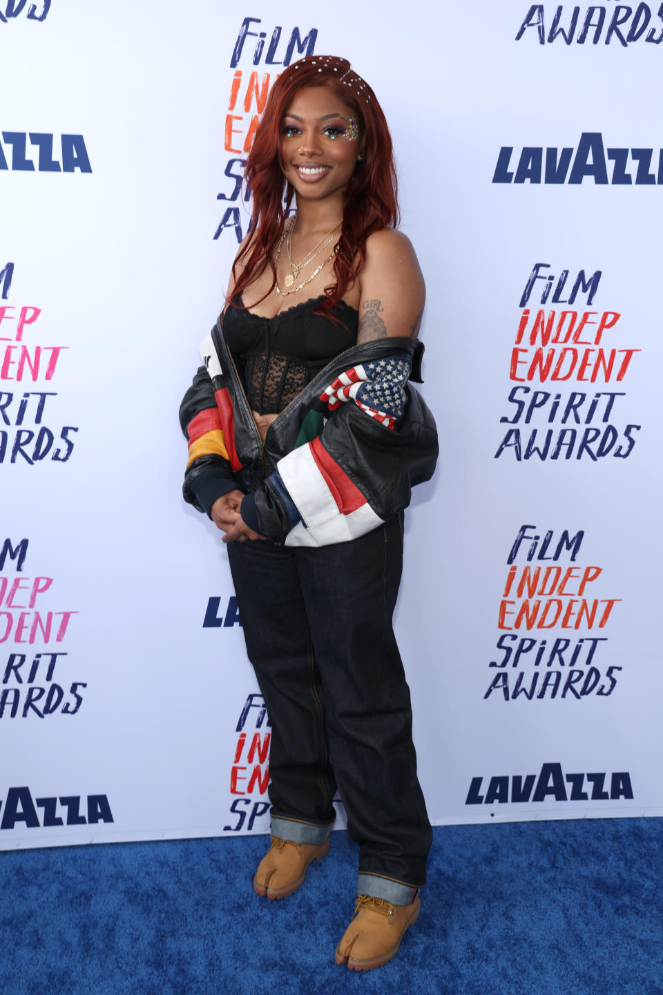 Tia on red carpet wearing a patchwork jacket, top, and hooved footwear