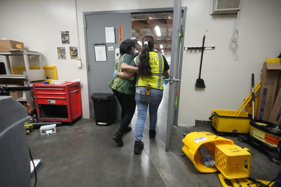 Los Angeles Food Bank custodian Maria Recinos, left, is found "safe" by a team member looking for people left behind inside the building, as they practice a "drop, cover, and hold on" simulation at a ShakeOut earthquake drill at the Los Angeles Regional Food Bank in Los Angeles Thursday, Oct. 19, 2023. Up and down the West Coast, the ShakeOut drill was scheduled to begin at 10:19 a.m. PDT with a cellphone-rattling test alert from the region's ShakeAlert earthquake warning system. (AP Photo/Damian Dovarganes)