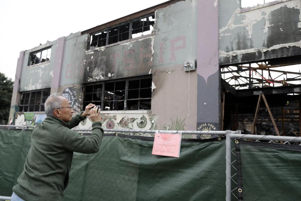 A man takes cell phone photos at the scene of a warehouse fire Tuesday, Dec. 13, 2016, in Oakland , Calif. The fire killed dozens of people during a electronic dance party as it raced through the building, in the deadliest structure fire in the U.S. in more than a decade. (AP Photo/Marcio Jose Sanchez)