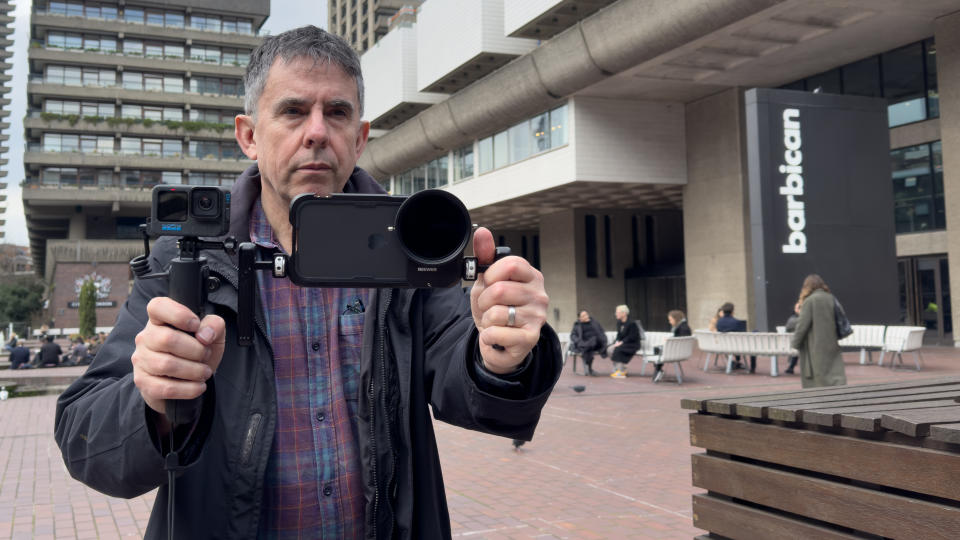 Man holding an iPhone in a cage and a GoPro next to each other in front of him