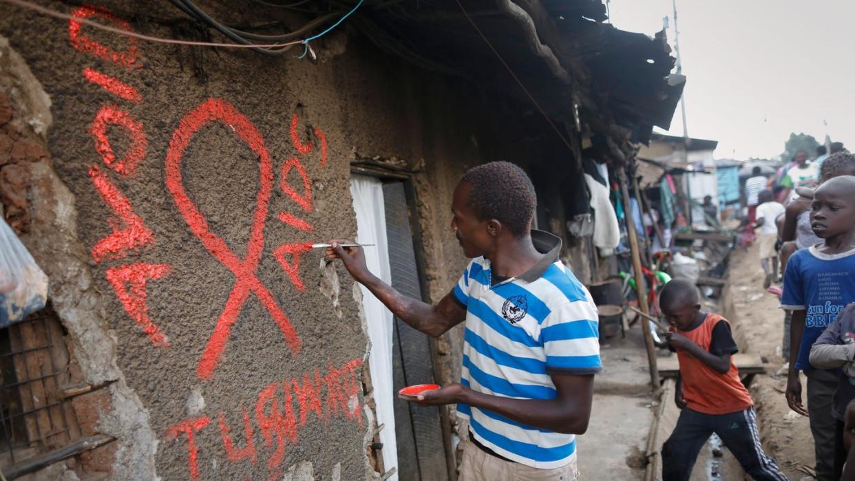 Ein junger Mann malt eine rote Aids-Schleife auf eine Wand im Kibera-Slum und schreibt in roten Buchstaben den Slogan «Avoid AIDS». Foto: Dai Kurokawa/EPA/Archiv