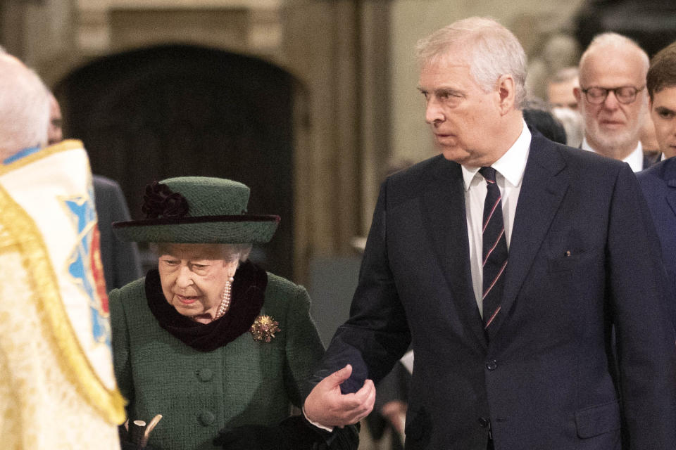 Queen Elizabeth II walks with son Prince Andrew, the Queen is wearing a green hat and green jacket. Prince Andrew has a black suit jacket on and a stripy tie. 