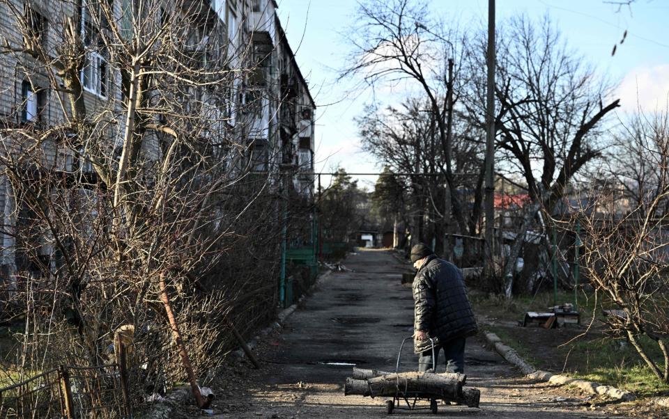 A local resident carries firewood in front of a damaged building in the town of Lyman in the Donetsk region - AFP