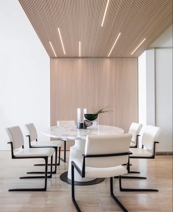 In the dining room of a Surfside apartment designed by Hino Studio, a Joseph Jeup marble table is surrounded by white leather Holly Hunt chairs. Custom Italian millwork with LED lights was installed across the ceiling.