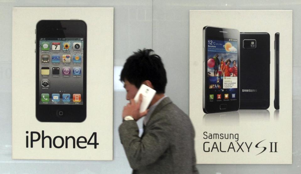 FILE - In this Nov. 22, 2013 file photo, a man walks past banners advertising smartphones by Samsung and Apple at a mobile phone shop in Seoul, South Korea. The high-stakes battle between the world's largest smartphone makers is scheduled to wrap up this week after a monthlong trial that has pulled the curtain back on just how very cutthroat the competition is between Apple and Samsung. Closing arguments in the patent-infringement case are scheduled to begin Monday, April 28, 2014 with the two tech giants accusing each other, once again, of ripping off designs and features. At stake: $2 billion if Samsung loses, a few hundred million if Apple loses. (AP Photo/Yonhap, Han Sang-kyun, File) KOREA OUT