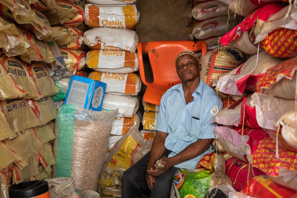 Vendor surrounded by bags of rice at a market.