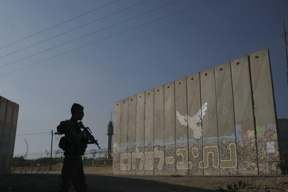 A member of Israeli forces stands next to a security wall with Hebrew writing reading "Path to Peace" at the Kibbutz Netiv Haasara near the border with Gaza Strip, Israel, Friday, Nov. 17, 2023. The kibbutz, located close to the Gaza Strip's separation fence with Israel, was attacked during the Hamas cross-border attack on Oct. 7, killing members of its community. (AP Photo/Leo Correa)