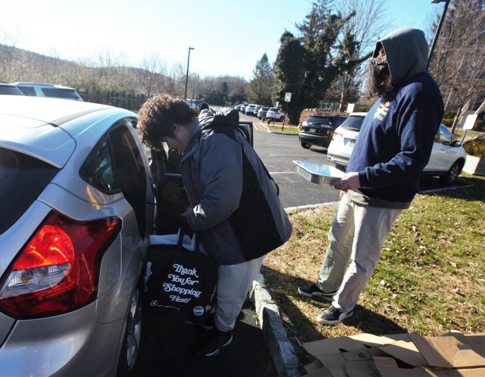 John Lupack, a New Jersey Youth Corps student, places bags filled with donated holiday food to a local family member in need, as another volunteer hands over a roaster pan, at Project Self-Sufficiency in Newton on Monday, Nov. 21, 2022.