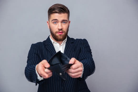 A well-dressed businessman holding open his empty wallet.