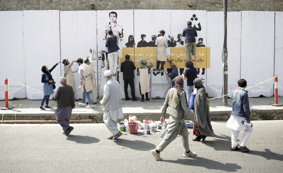 Residents walk past artists from ArtLords organizationas they paint a mural of journalists who have been killed during the year of 2018, in Kabul, Afghanistan, Tuesday, Sept. 25, 2018. It's the first in a series of murals planned by Amnesty International and the Artlords collective to highlight the work of Afghan activists, teachers, lawyers, students, trade unionists and others. (AP Photo/Massoud Hossaini)