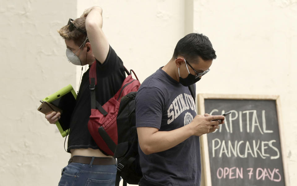 Pedestrians wear masks as smoke shrouds the Australian capital of Canberra, Australia, Thursday, Jan. 2, 2020. Australia deployed military ships and aircraft to help communities ravaged by apocalyptic wildfires that destroyed homes and sent thousands of residents and holidaymakers fleeing to the shoreline. (AP Photo/Mark Baker)