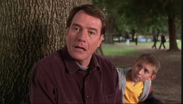 Bryan Cranston and Erik Per Sullivan sit by a tree in a park, looking surprised