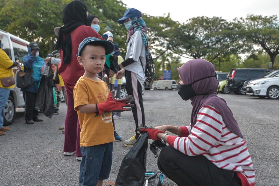 Ili Syairah (right) and her three-year-old son don gloves and other protective gear before setting out to pick up trash. — Picture by Shafwan Zaidon