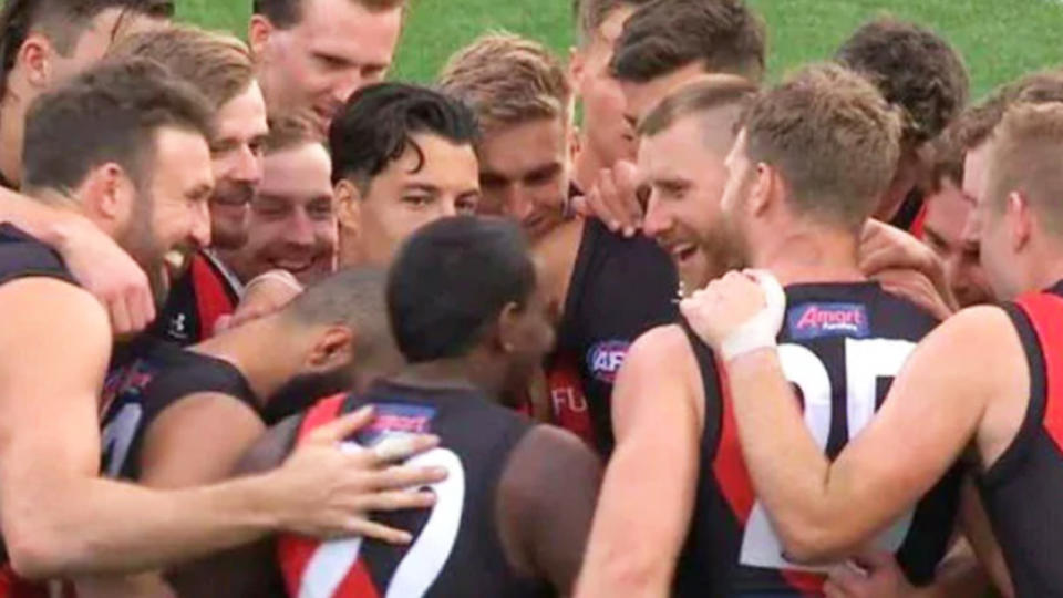 Essendon players laugh at a joke in a team huddle.