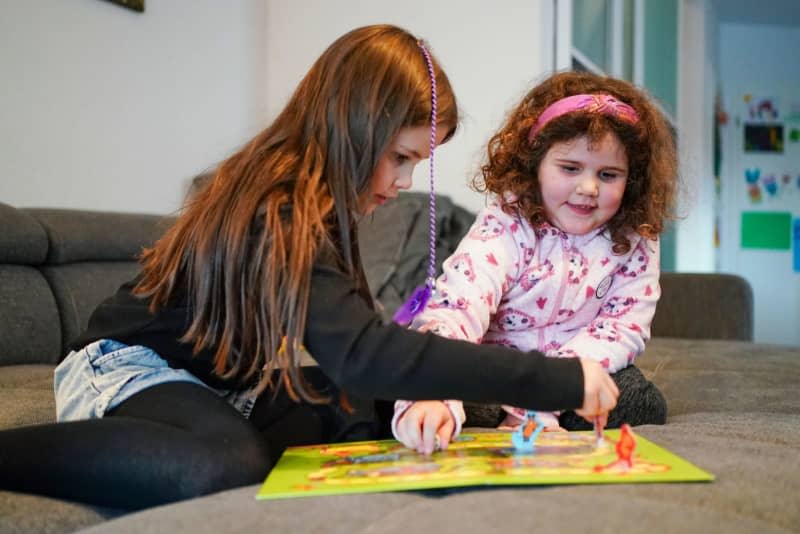 Six-year-old Enna (r) and her sister Luisa play a board game in the living room. Shortly before Enna's fourth birthday, she was diagnosed with a brain tumour. The fight against cancer is particularly difficult in children, with often no suitable medication available. However, some tumours have weak points that doctors can target - as was Enna's case. Uwe Anspach/dpa