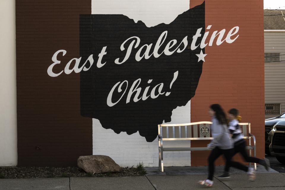 Children run past a mural in East Palestine, Ohio, Tuesday, March 7, 2023. Almost 3 months after a fiery Norfolk Southern train derailment blackened the skies, sent residents fleeing and thrust East Palestine into a national debate over rail safety, residents say they are still living in limbo. (AP Photo/Matt Rourke)