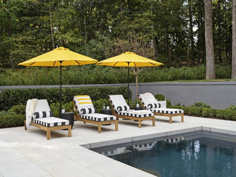 cabana at the far end of the pool, bright yellow umbrellas over four teak chaises welcome guests to stay awhile chic black and white outdoor fabric cushions dry in a snap after a day of of splashing and lounging