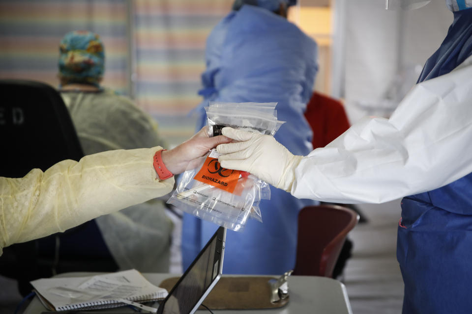 Catherine Hopkins, Director of Community Outreach and School Health at St. Joseph's Hospital, right, hands a batch of COVID-19 samples to an assistant in a testing tent, Monday, April 20, 2020, in Yonkers, N.Y. (AP Photo/John Minchillo)