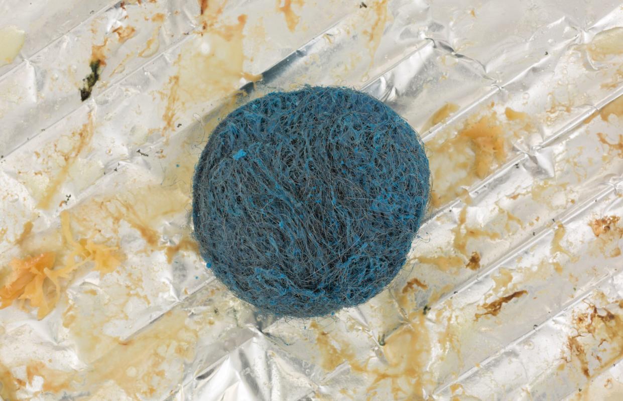 Top view of a stainless steel soap scouring pad atop a greasy tinfoil covering a wire rack.