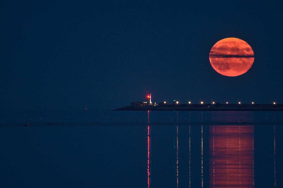 Rare summer full blue sturgeon Moon rising over Irish sky between Dun Laoghaire lighthouses on August 23, 2021 seen from Sandymount Beach, Dublin, Ireland