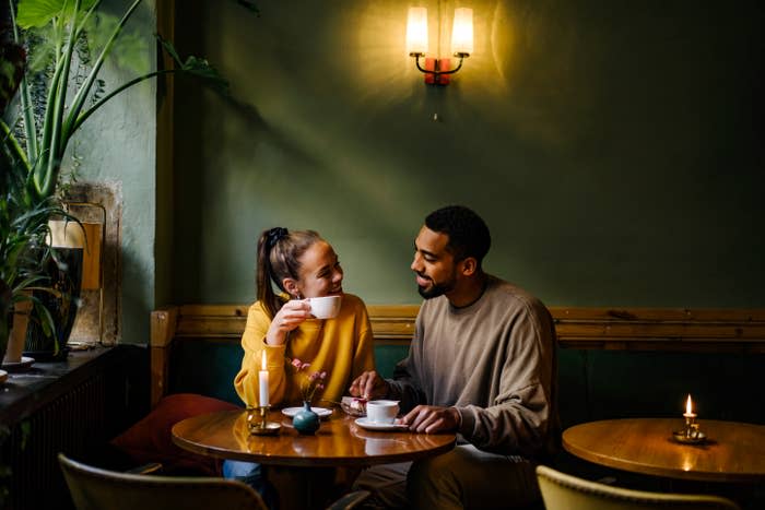 Two people smiling at each other at a cafe table with beverages and a dessert