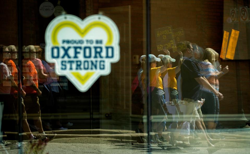 Reflected in some of the Oxford Strong signs in business windows in downtown Oxford, marchers carry signs and chant as they march in the March For Our Lives Oxford event on Saturday, June 11.