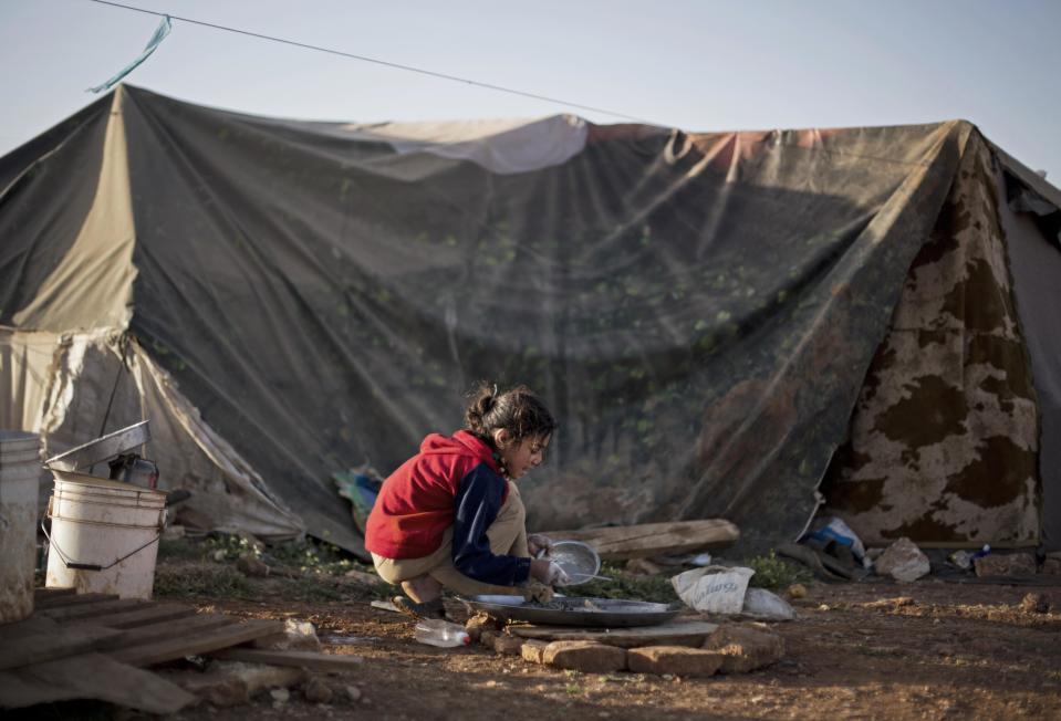 In this Tuesday, April 8, 2014 photo, a Syrian refugee girl washes dishes in front of her family tent in an unofficial refugee camp on the outskirts of Amman, Jordan. Some residents, frustrated with Zaatari, the region's largest camp for Syrian refugees, set up new, informal camps on open lands, to escape tensions and get closer to possible job opportunities.(AP Photo/Khalil Hamra)