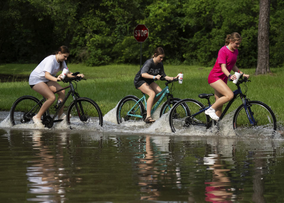 Girls ride their bikes through flood water near the bridge over Lake Houston along West Lake Houston Parkway after it was closed due to high water on either side of the thoroughfare, Saturday, May 4, 2024, in Kingwood, Texas. (Jason Fochtman/Houston Chronicle via AP)