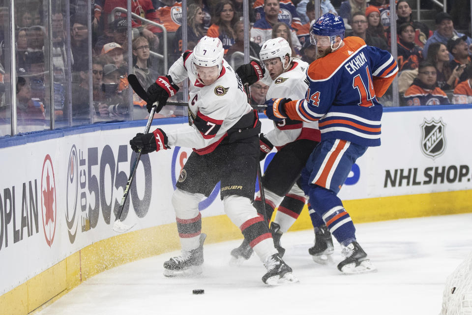Ottawa Senators' Brady Tkachuk (7) and Josh Norris (9) and Edmonton Oilers' Mattias Ekholm (14) compete for the puck during the first period of an NHL hockey game Saturday, Jan. 6, 2024, in Edmonton, Alberta. (Jason Franson/The Canadian Press via AP)