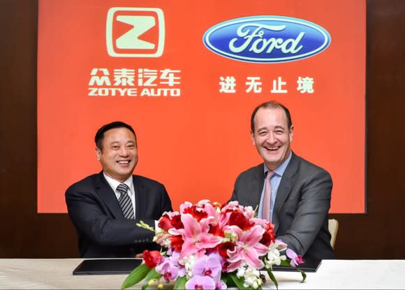 Fleet and Ying are seated at a table in front of a red banner with the Zotye Auto and Ford logos.