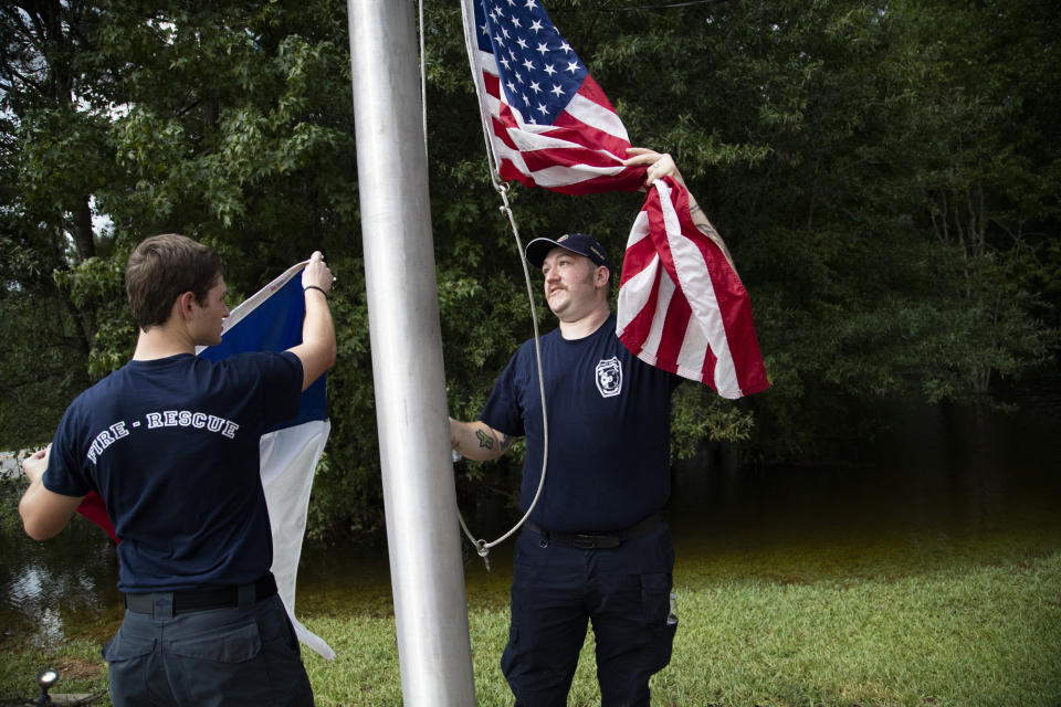 Caney Creek Fire Department firefighters Avery Aultman, 21, left, Luke Hancock, 24, right, raise the United States flag and the Texan flag while cleaning up the fire station on Friday, Sept. 20, 2019, in Conroe, Texas, after it got flooded on Thursday. Floodwaters are starting to recede in most of the Houston area after the remnants of Tropical Storm Imelda flooded parts of Texas. (Marie D. De Jesus/Houston Chronicle via AP)